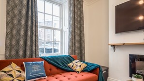 Een woonkamer met een rode bank, gestreepte kussens, een turquoise plaid en een open haard.