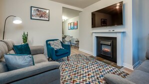 Ein modernes Wohnzimmer mit Kamin, großem Flachbildfernseher und blauem Sessel.