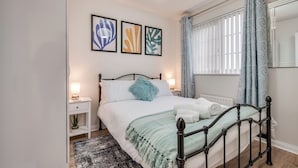Ein Schlafzimmer mit Bett, Nachttischen, einer Lampe, einer Pflanze und Kunstwerken an der Wand.
