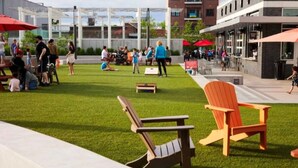 An outdoor seating area with green artificial turf, wooden Adirondack chairs, and red umbrellas. - Covered patio, finished basement, amazing location (Overland Park)