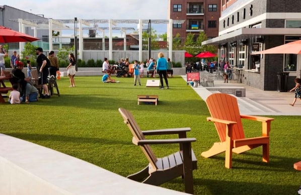 An outdoor seating area with green artificial turf, wooden Adirondack chairs, and red umbrellas.