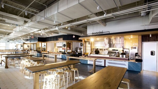A spacious cafe with multiple wooden tables and stools, a visible counter area, and a high ceiling with exposed ductwork. - Covered patio, finished basement, amazing location (Overland Park)
