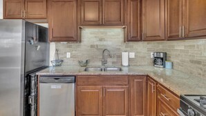 A kitchen with wooden cabinets, a stainless steel refrigerator, a dishwasher, a sink, and a coffee maker. - Covered patio, finished basement, amazing location (Overland Park)