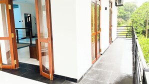 A corridor with a wooden door leading to a room, a balcony with a metal railing, and an air conditioning unit on the wall. - Galle Nature Nook (Galle)