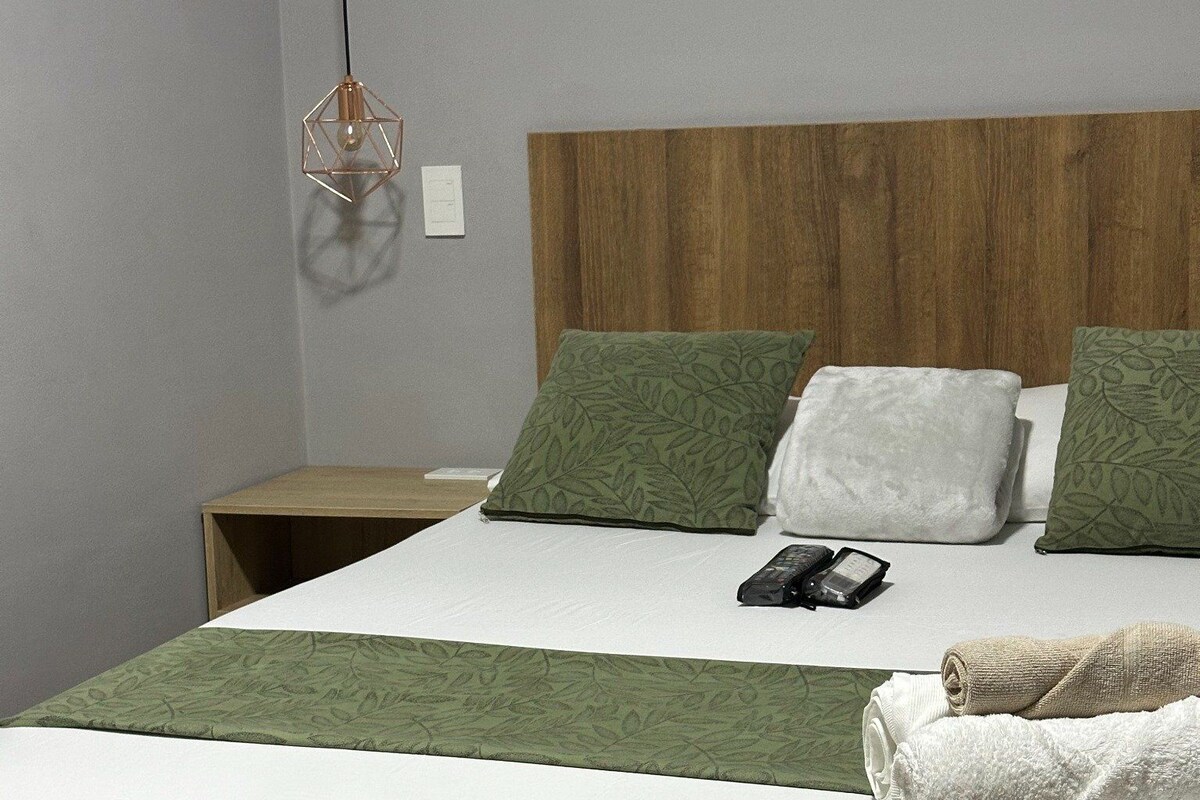 A neatly made bed with a green bedspread, two pillows, and a remote control on the bed.