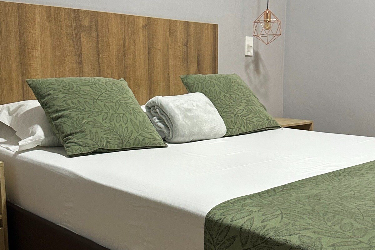 Una cama bien hecha con cabecera de madera, almohadas estampadas en verde y colcha blanca.