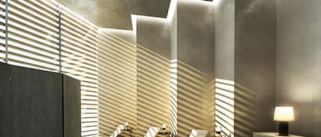 Un moderno espacio de spa con sillones reclinables, una lámpara de pared y grandes ventanales con persianas.