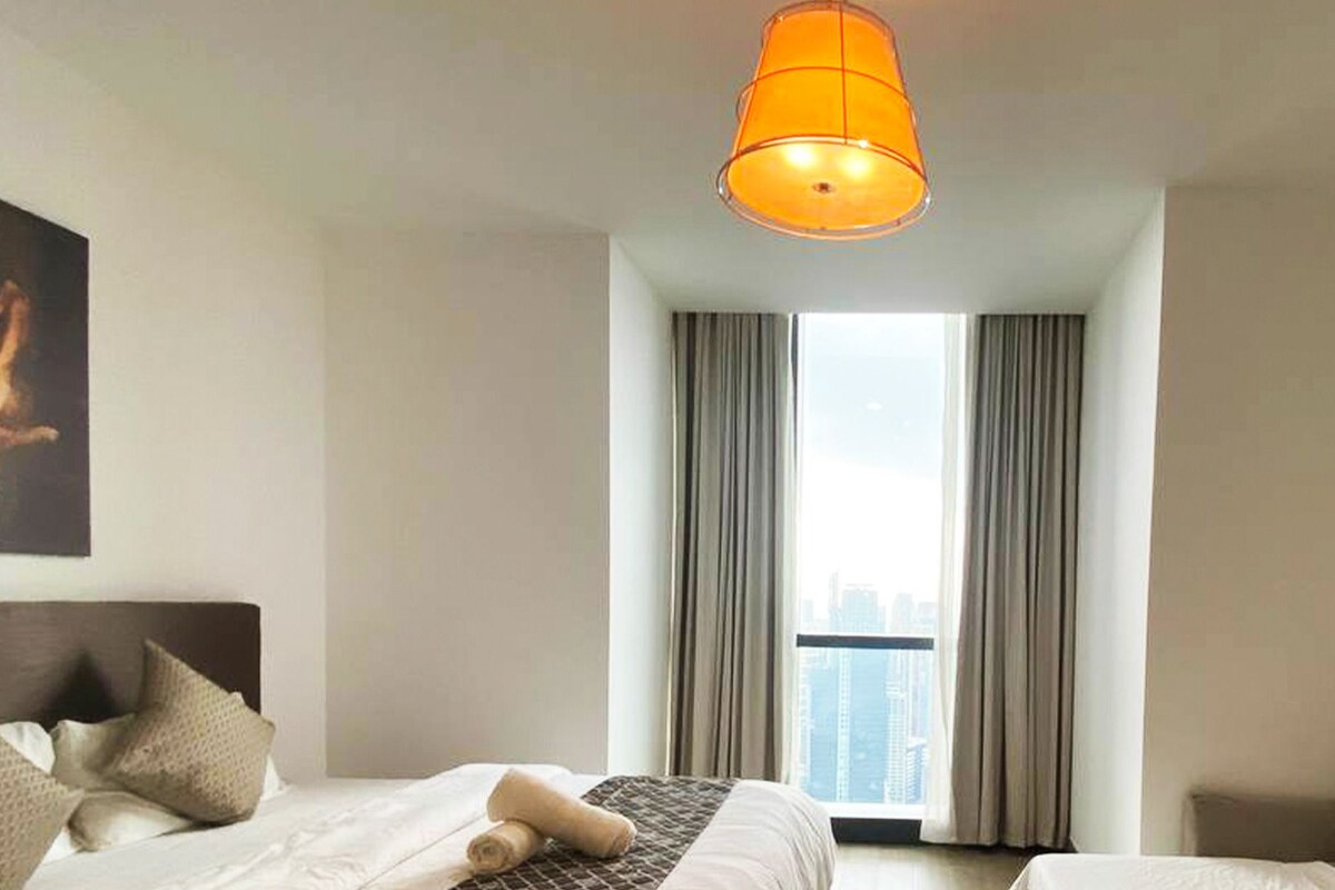 A hotel room with two beds, a sofa bed, a large window with curtains, and a city view.