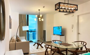 A modern living room with a glass table, a sofa, a TV, and a view of the city.