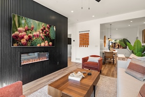 A modern living room with a flat-screen TV, a fireplace, a red sofa, and a dining area with a wooden table and chairs.