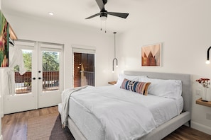 A bedroom with a bed, a ceiling fan, a nightstand, a wall-mounted light, and a door leading to an outdoor area.