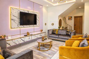 Ein modernes Wohnzimmer mit Marmorwand, einem Flachbildfernseher, einer Couch und einem gelben Sessel.