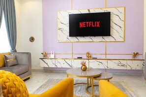 Ein Wohnzimmer mit einer Couch, einem Couchtisch und einem an der Wand befestigten Fernseher, der 'NETFLIX' zeigt.