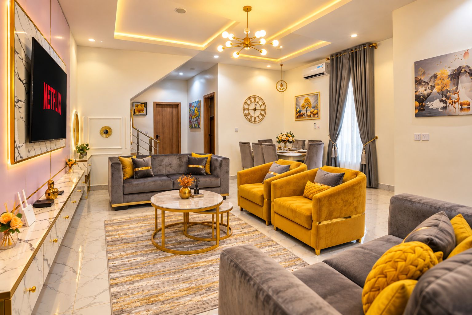 A modern living room with a sofa, armchairs, a coffee table, and a TV mounted on the wall.
