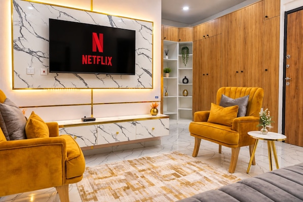 A modern living room with a marble wall, a Netflix TV, a wooden cabinet, and a yellow armchair.