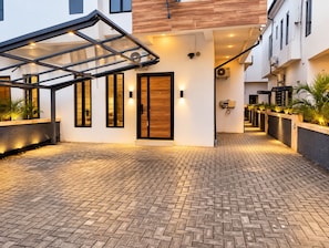 Un edificio moderno con entrada de vidrio, un patio empedrado con ladrillos y una puerta de madera.