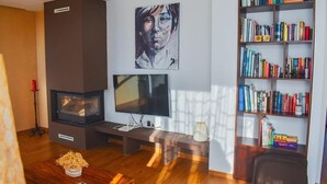 Ein Wohnzimmer mit Kamin, Flachbildfernseher, Bücherregal und einem Gemälde an der Wand.