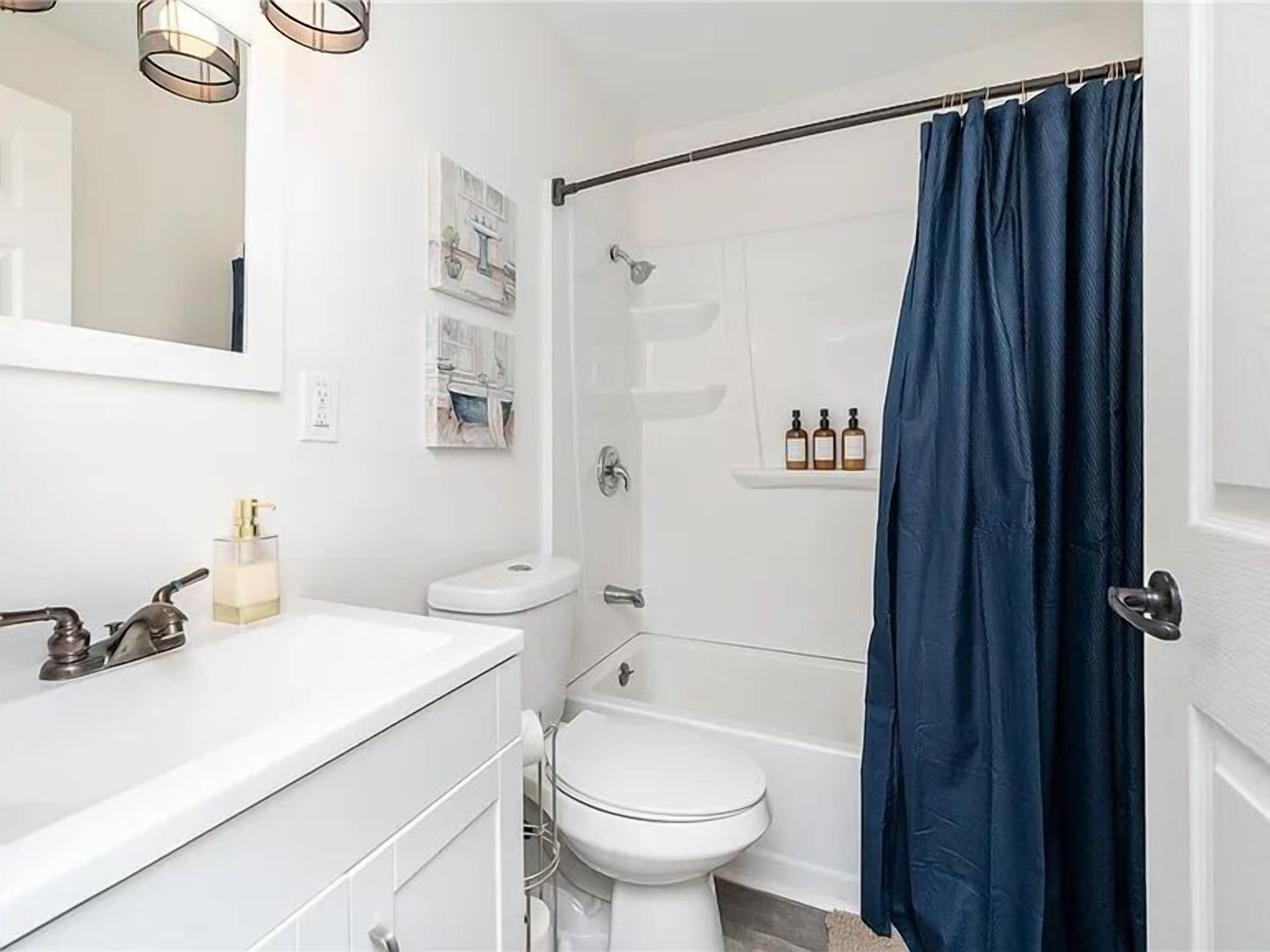 A modern bathroom with a white vanity, a toilet, a bathtub, and a shower curtain.