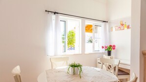 Una habitació lluminosa amb una taula rodona, cadires blanques i una planta en test.
