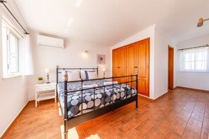 Un dormitori amb un llit, una tauleta de nit, una planta en test i un armari de fusta.