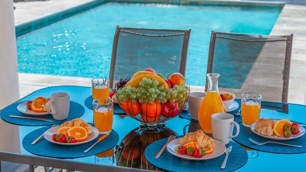 Taula de l'esmorzar amb fruita, suc i croissants vora una piscina.