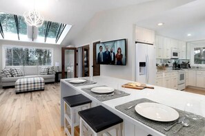 Een moderne keuken met een centraal eiland, witte kastjes en een groot raam met uitzicht op een bos.