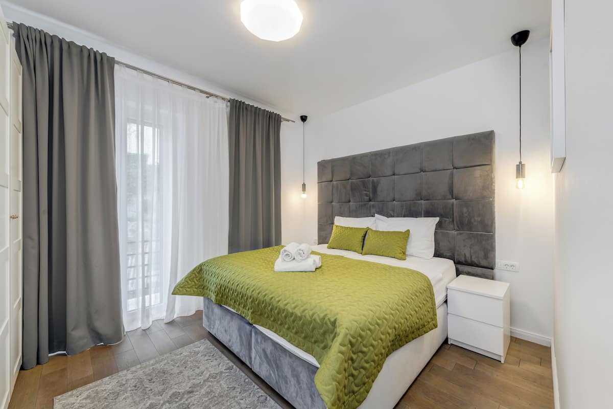 A modern bedroom with a large bed, grey curtains, a bedside table, and a headboard.