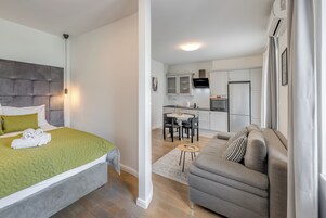 Een moderne slaapkamer met een bed, een grijze bank en een klein zithoekje met een tafel en stoelen.