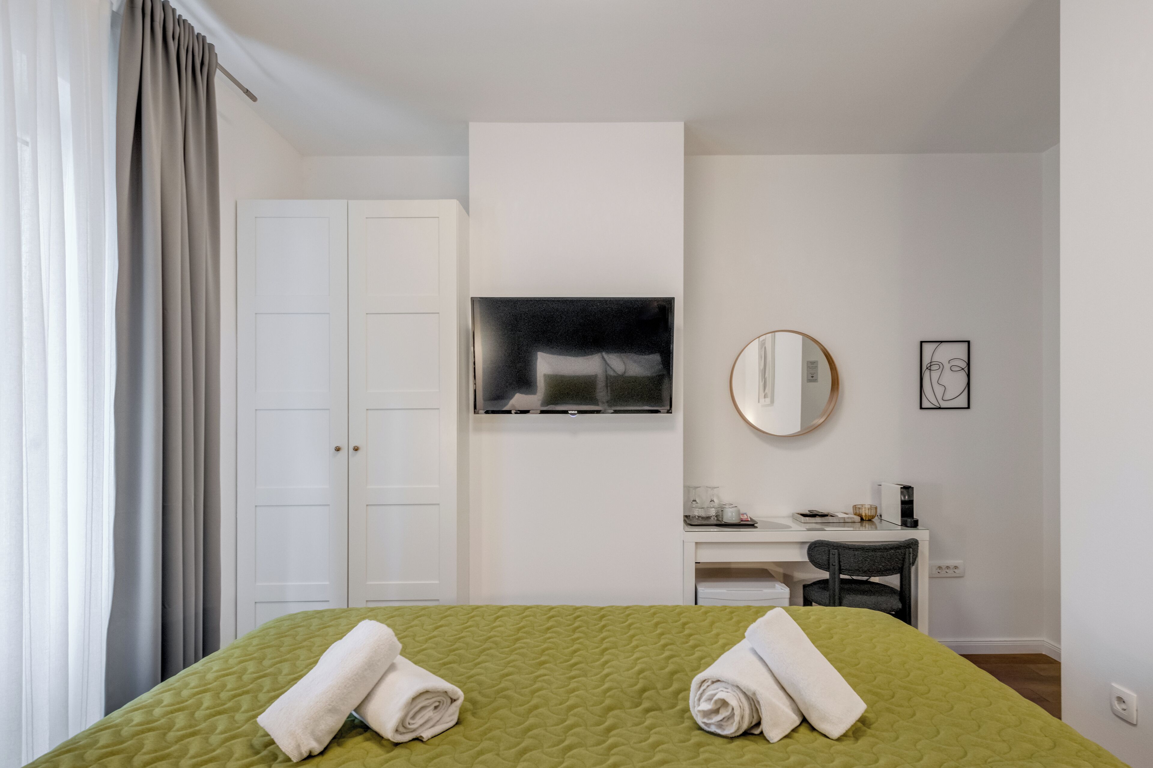 Une chambre d’hôtel comprenant un lit, un bureau, une chaise, une télévision, un miroir et un tableau encadré accroché au mur.