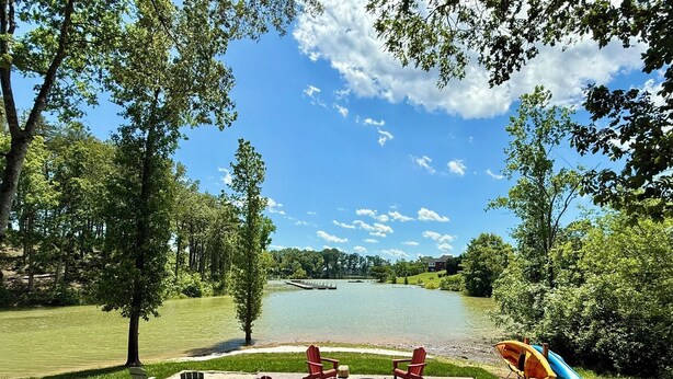 A lakeside patio with Adirondack chairs, a fire pit, and a paddle boat.