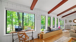 A spacious room with large windows, a wooden desk, a comfortable seating area, and a view of a forest.