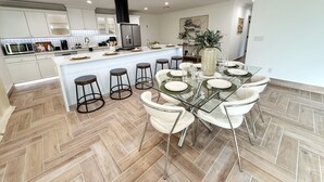 A modern kitchen with white cabinets, a central island, and a dining area with a glass table and white chairs.