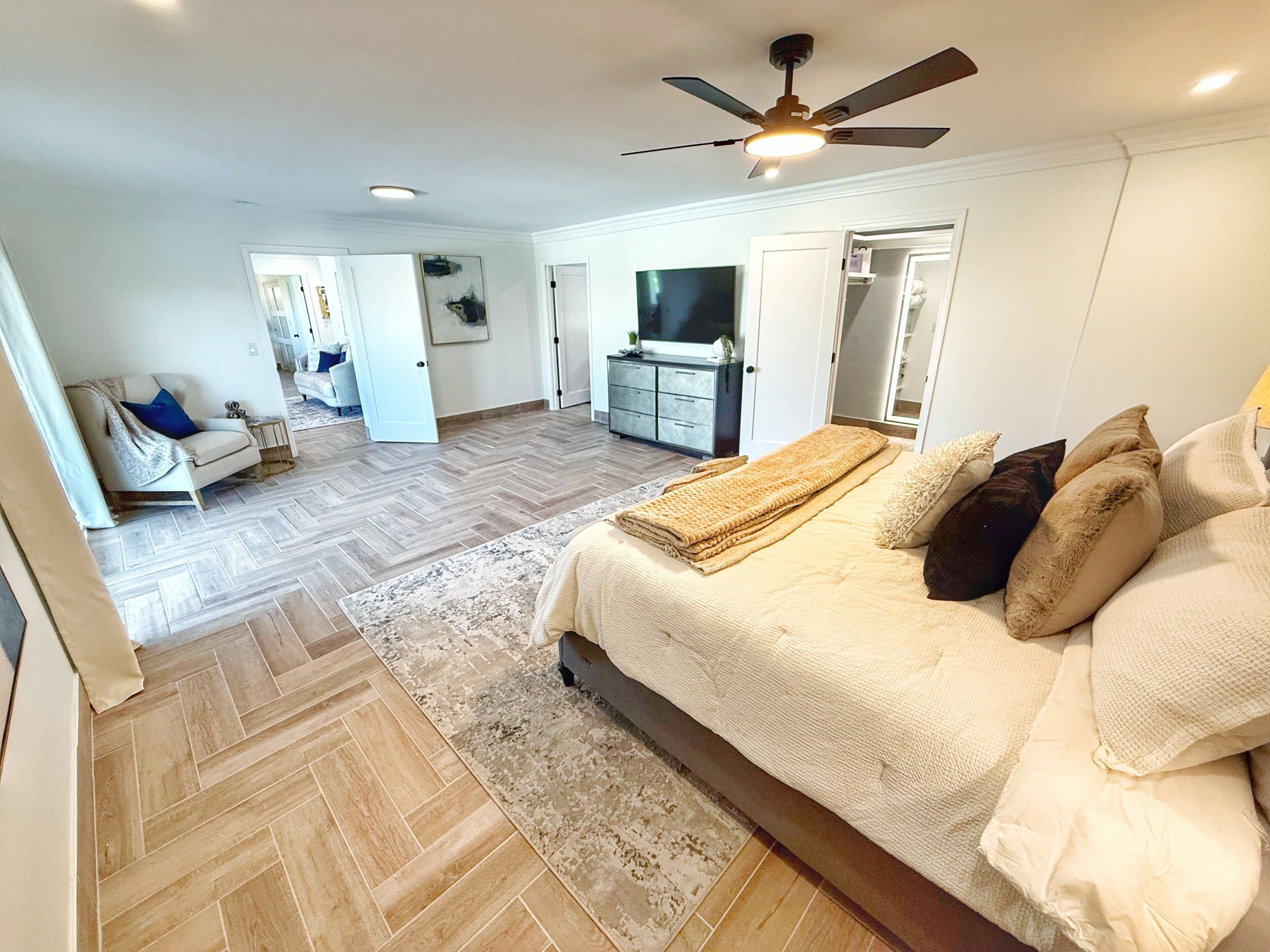 Une chambre spacieuse avec un grand lit, un ventilateur de plafond et un téléviseur.