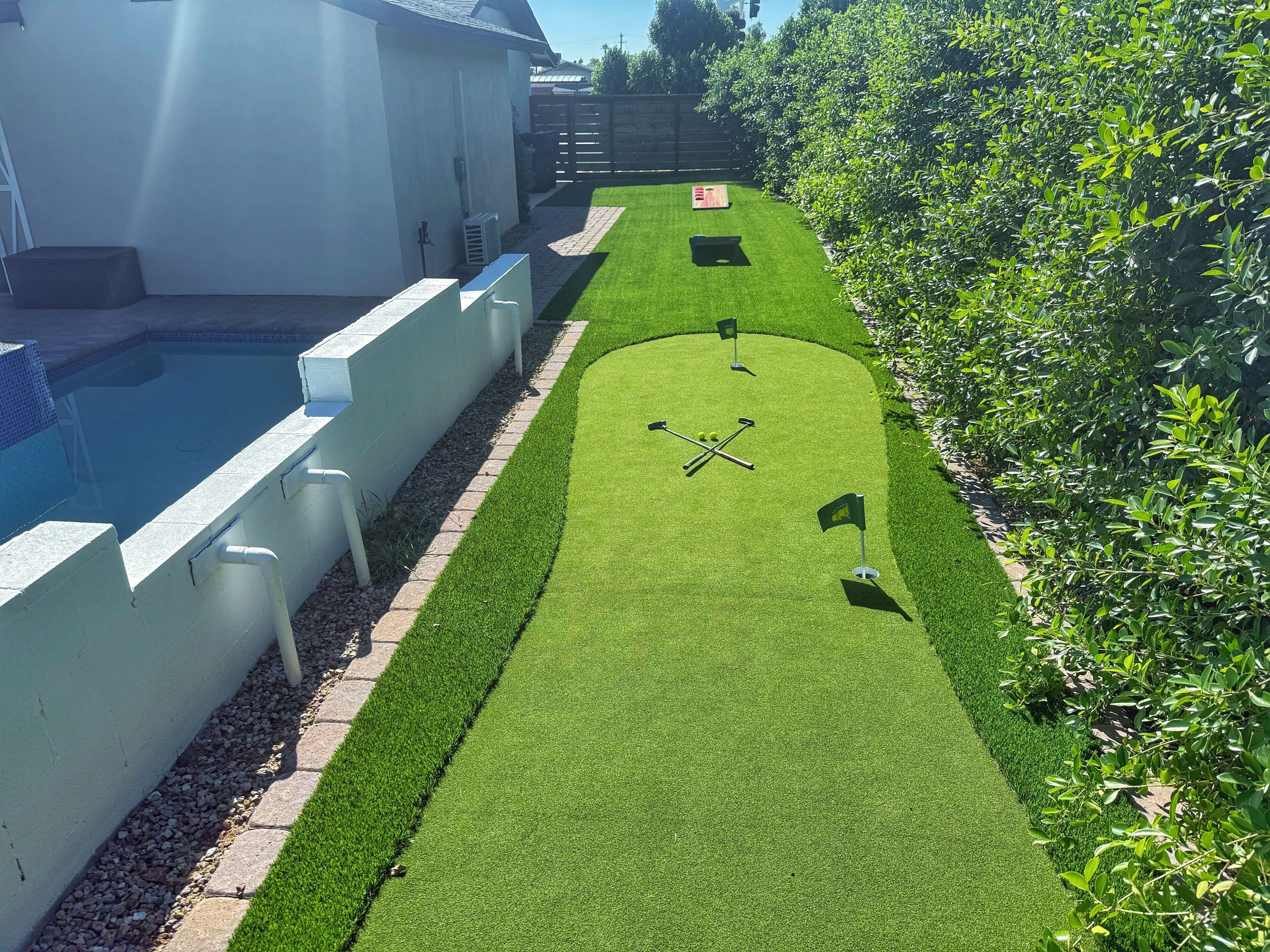 A well-maintained lawn with a putting green, a pool, and a hedge.
