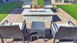 An outdoor patio with a stone fire pit, wicker furniture, and a grill.