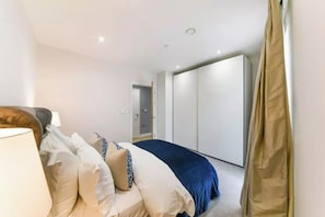 A bedroom with a bed, pillows, a lamp, a wardrobe, and a door leading to another room. - 2 Bed | Canary Wharf | Stunning Views (London)