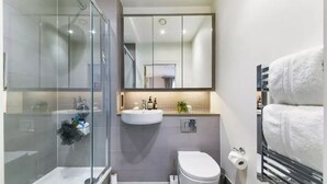 A modern bathroom with a glass shower enclosure, a white sink, a toilet, and a towel rack. - 2 Bed | Canary Wharf | Stunning Views (London)
