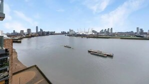 A river with boats, a city skyline, and a building with a balcony. - 2 Bed | Canary Wharf | Stunning Views (London)