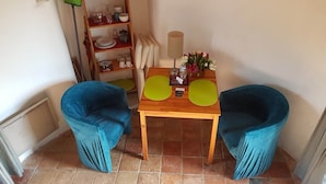 A small dining area with two blue chairs, a wooden table, and a shelf with kitchenware.