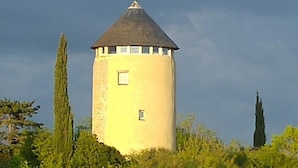 A cylindrical tower with a conical roof, surrounded by greenery.