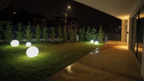 A nighttime view of a modern outdoor area with a paved walkway, illuminated spherical lights, and neatly trimmed grass. - Belleview Cluj (Cluj-Napoca)