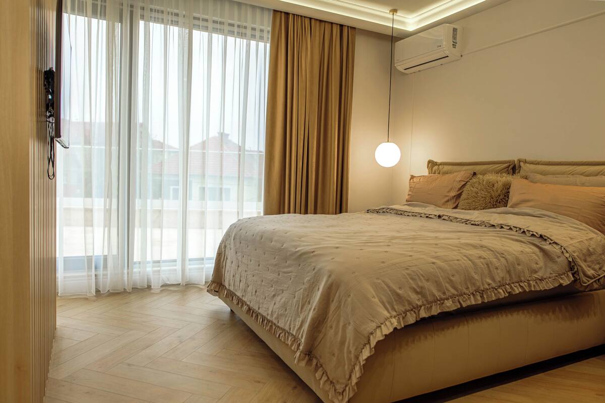 Un dormitorio con cama, cortinas, unidad de aire acondicionado y lámpara colgante.