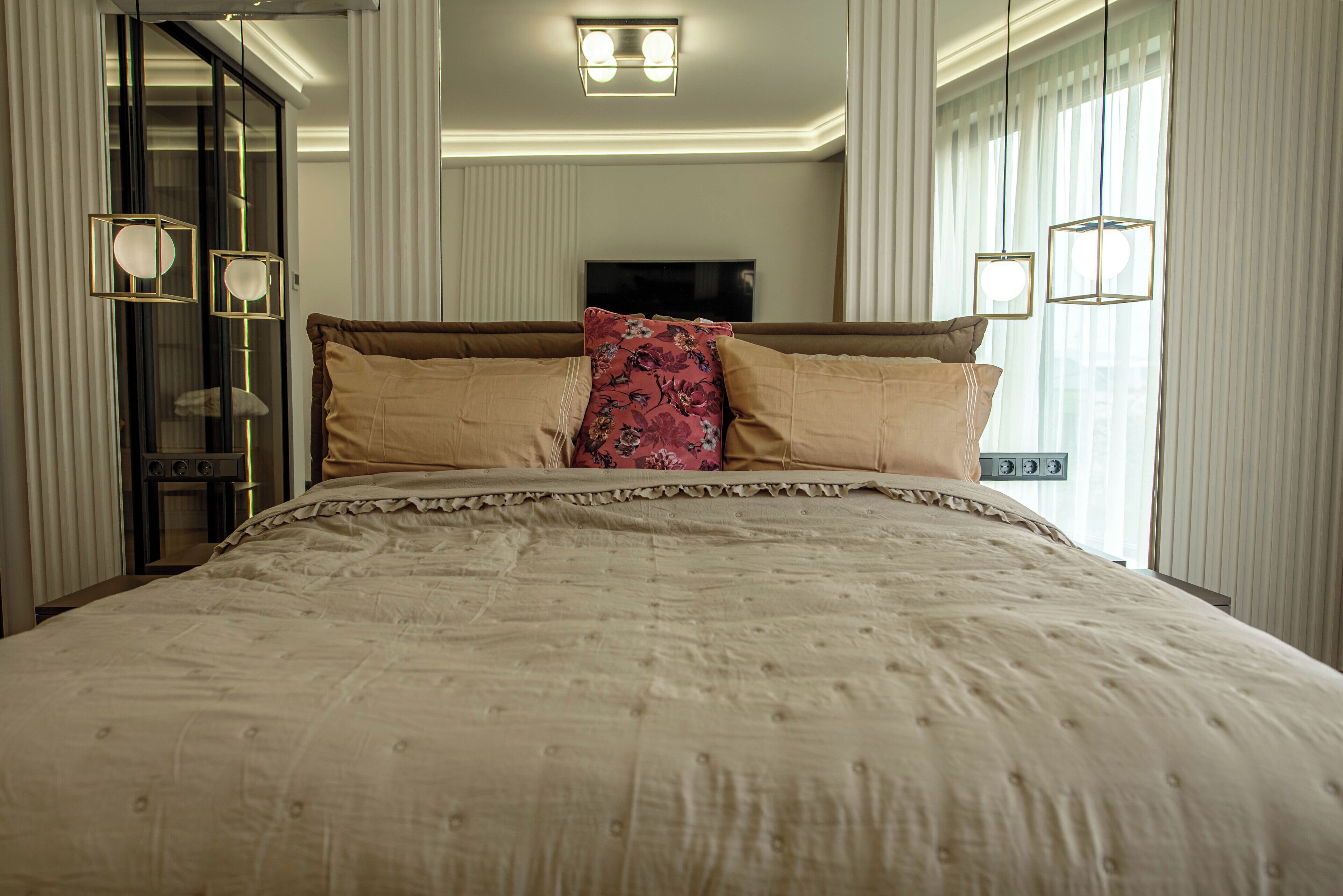 Een groot bed met een bloemenkussen, een televisie erboven en een schuifdeur aan de linkerkant.