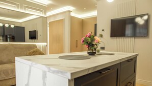A modern kitchen with a marble countertop, built-in cabinets, and a flat-screen TV mounted on the wall. - Belleview Cluj (Cluj-Napoca)