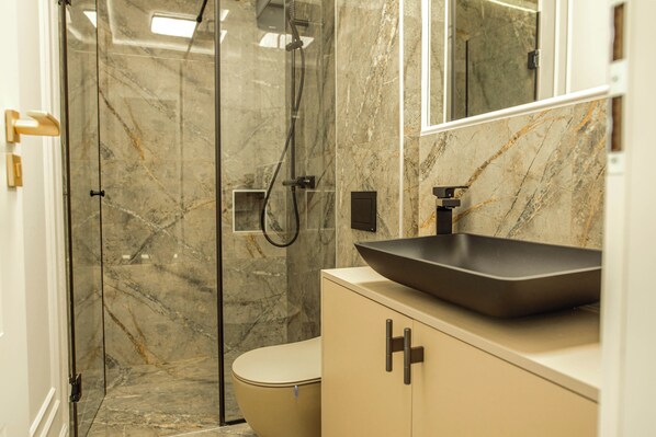 A bathroom with a marble shower, a toilet, and a sink with a large basin. - Belleview Cluj (Cluj-Napoca)