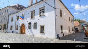 A historic building with a cobblestone street, a wooden door, and a flag. - Belleview Cluj (Cluj-Napoca)