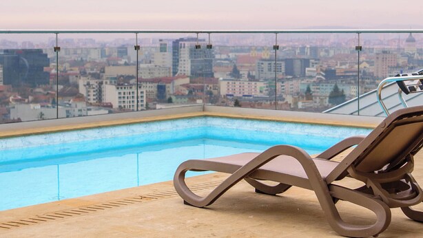 A rooftop pool with a city view, a lounge chair, and a glass railing. - Belleview Cluj (Cluj-Napoca)