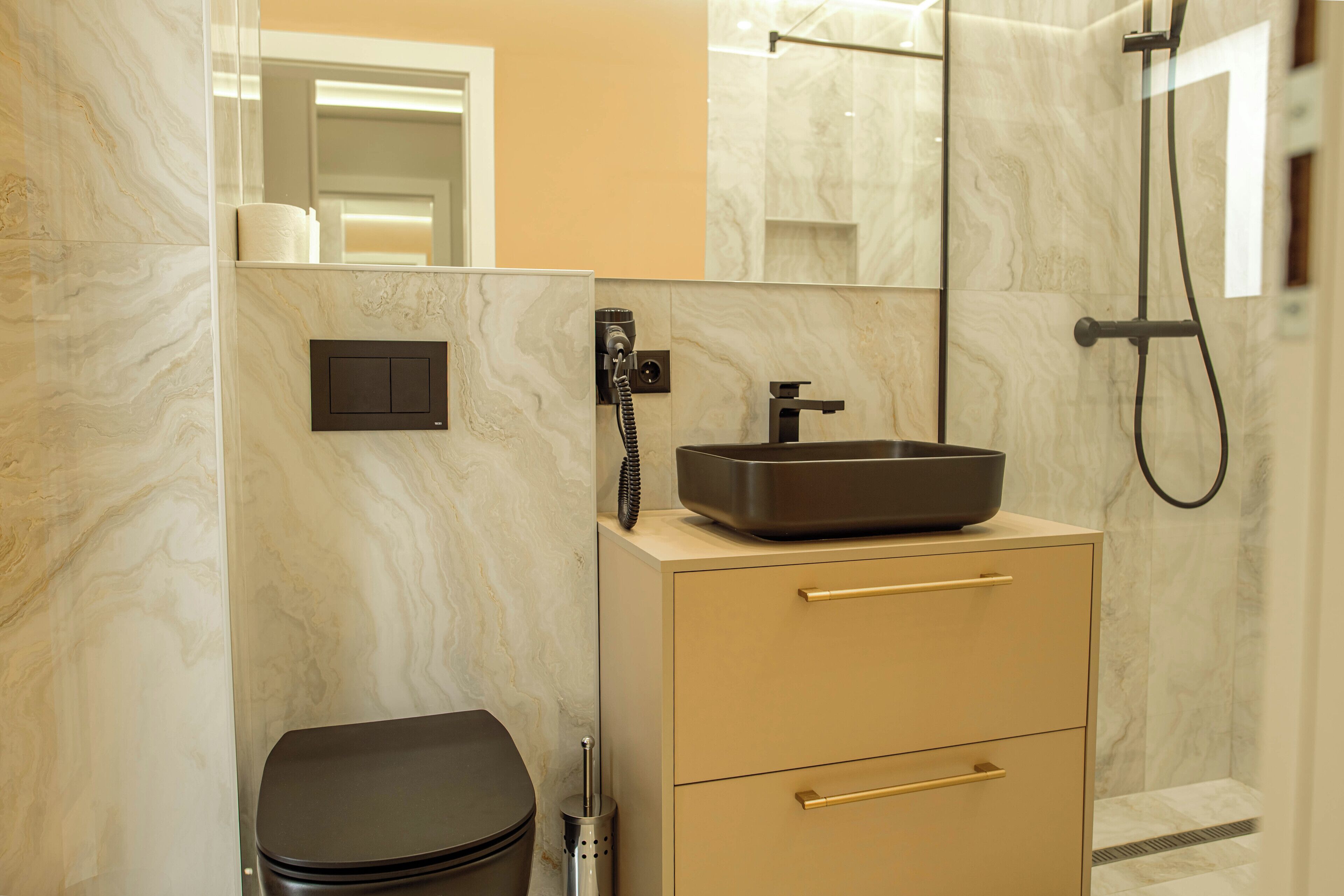 A modern bathroom with a marble wall, a black sink, a toilet, and a shower.