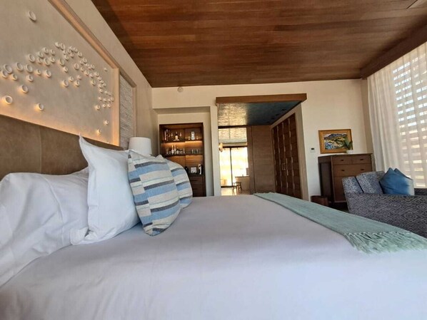 Une chambre avec un grand lit, un plafond en bois, une étagère intégrée où sont rangées des bouteilles, et une vue sur la pièce.