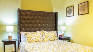 A neatly made bed with a patterned bedspread, two bedside tables with lamps, and framed botanical artwork on the wall.